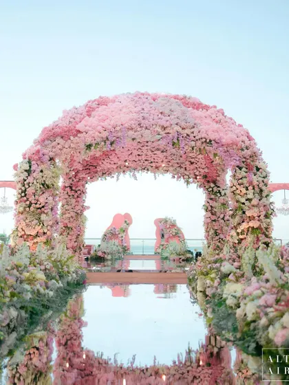 The 'Echoes of Pink' mandap, a stunning floral arch set against the sea in Doha. Adorned with thousands of flowers, it signifies the blooming of a new relationship, with a mirrored aisle reflecting the sky.