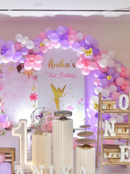For this fairy-themed first birthday, I used a soft palette of pink, purple, and white balloons to create a dreamy arch. The decor is personalized with light-up numbers and the baby's name.