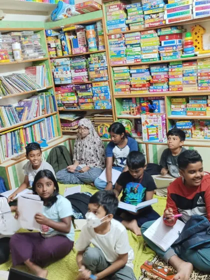 A group of students engaged in a public speaking session, surrounded by books. The library provides a wonderfully inspiring backdrop for learning.