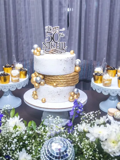 A chic and modern dessert table for a 50th birthday bash. Our two-tier white and gold cake, featuring a rope texture and metallic spheres, was the star of the show.