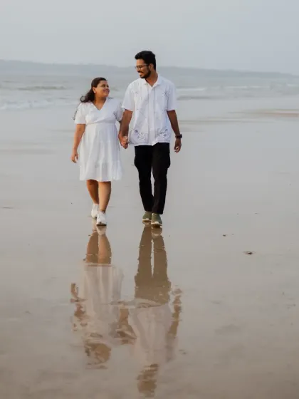 A beautiful reflection shot of the couple walking on the wet sand at sunset. This composition adds an artistic and serene quality to the pre-wedding album.
