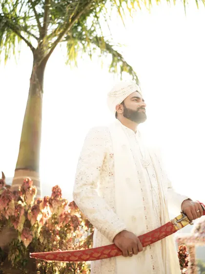 The groom stands tall and proud with a ceremonial sword, bathed in the morning sun.