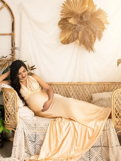 A serene solo portrait in the boho corner. The expecting mother reclines on the wicker sofa, bathed in a warm, sunny light, creating a tranquil and beautiful image.