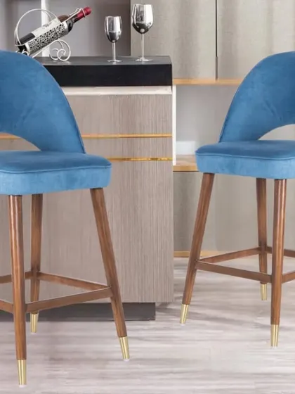 These wooden bar stools feature a comfortable, upholstered seat in blue fabric and gold-tipped legs. They are perfect for adding a pop of color to a kitchen counter or bar.