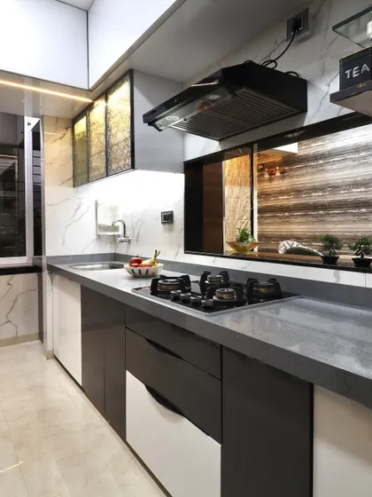 A modern kitchen design featuring a serving window that opens into the dining area. The kitchen has dual-tone cabinets, a grey quartz countertop, and textured glass overhead units with internal lighting.