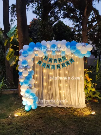 A simple and elegant balloon arch with a fairy light curtain, set up outdoors in a garden. This is perfect for an evening celebration.