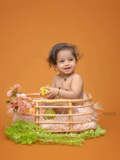 A happy baby boy playing in a wicker basket decorated with flowers and greenery. This is a classic and adorable setup for capturing baby's first few months.