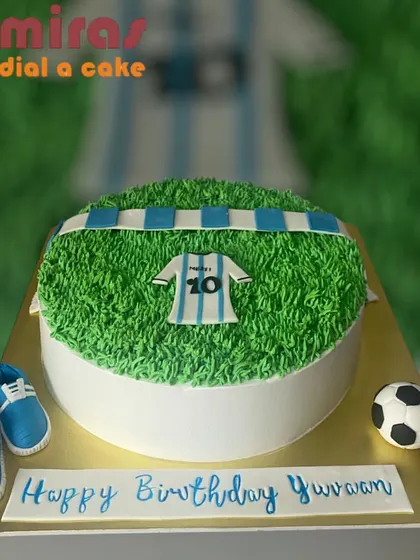 A football field cake complete with a jersey, soccer ball, and tiny shoes. This design is perfect for celebrating a young football player's birthday.