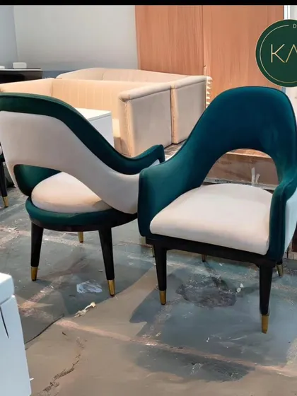 Two of our open-back dining chairs, seen here in our workshop. The combination of rich green velvet and off-white fabric, along with gold-tipped legs, showcases a design that is both luxurious and modern.