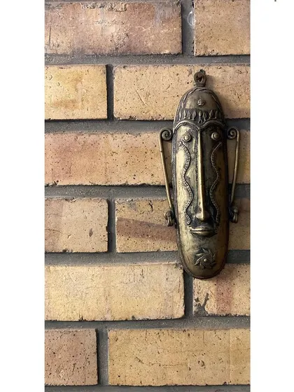 A handcrafted metal mask hangs on an exposed brick wall in our studio. We surround ourselves with art and artifacts that celebrate material, texture, and cultural expression.