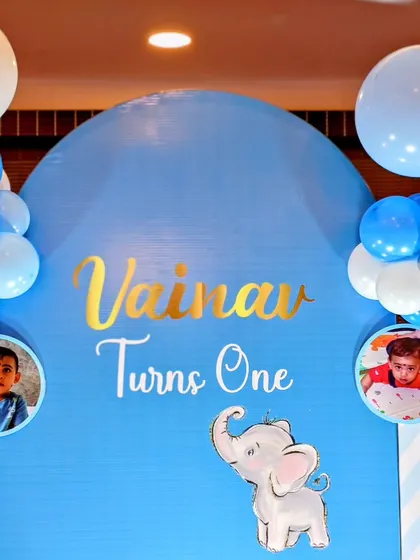 A personalized baby elephant theme for Vainav's first birthday. The arched blue backdrop features his name in gold script and includes small photos of the birthday boy.