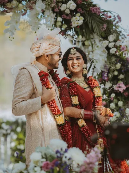 A joyful candid shot of the couple during their wedding ceremony, their smiles radiating happiness under a beautiful floral arch.