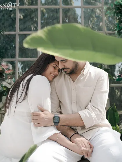 A tender moment captured in a sun-drenched greenhouse. The soft light and abundance of plants create a serene and intimate setting, with the large leaf providing beautiful natural framing.