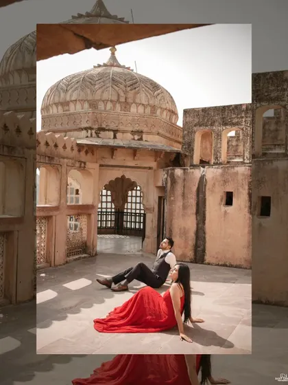 The couple relaxes on a sunlit terrace at Amer Fort, with the woman in a flowing red dress that provides a stunning contrast to the fort's sandstone architecture.