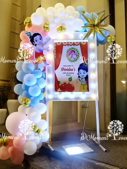 A beautiful welcome sign for a Krishna-themed party, illuminated with marquee lights and surrounded by a cloud of pastel balloons.