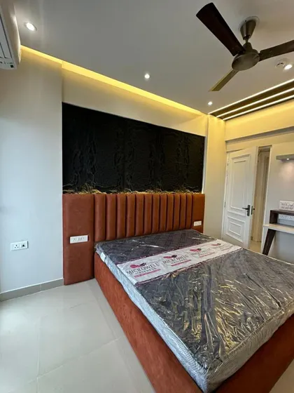 A contemporary bedroom featuring a custom bed with a channel-tufted, rust-colored velvet headboard. The bed is set against a dramatic black textured wall panel, creating a bold contrast and a luxurious feel.