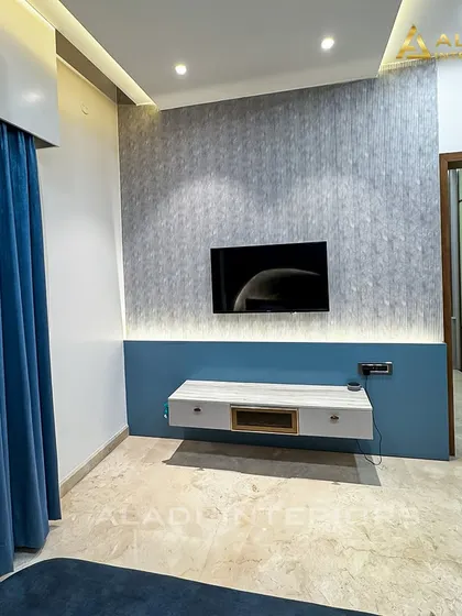 A bedroom with a cool blue and grey color palette. The floating TV console and textured wallpaper add a modern touch, while the blue curtains provide a pop of color.