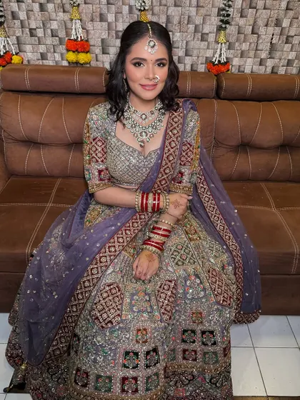 A full view of the bride on a couch, showing the beautiful flare and intricate patterns of her unconventional bridal lehenga.