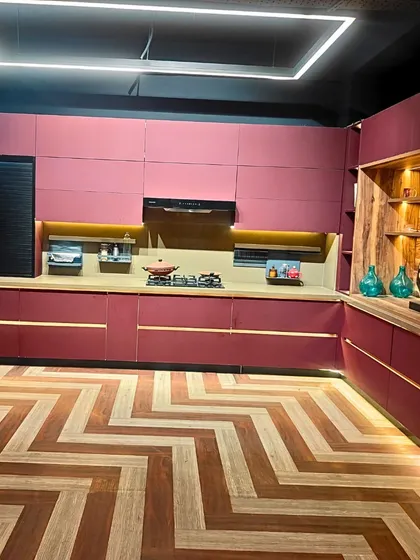 We love it when clients are not afraid to use color. This L-shaped modular kitchen showcases a bold and beautiful magenta finish, perfectly balanced with natural wood open shelving. The chevron-patterned flooring and integrated LED lighting in the cabinetry create a space that is vibrant, modern, and full of personality.