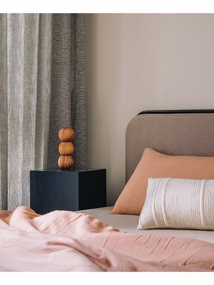 We love playing with color and texture. This bedroom features a custom headboard in a purple yam tone, paired with tangerine bedding. The colors blend effortlessly with the warm sand walls and the minimalist black bedside cube.