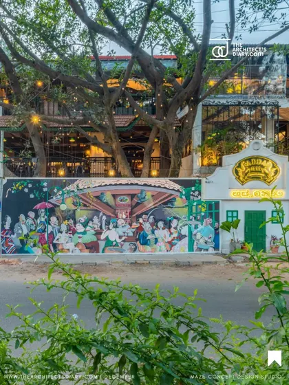 The exterior of Adda 1522 at night, showcasing a large, vibrant mural that captures the spirit of Bangalore. The design respects the existing trees on the property, integrating the building with its natural surroundings.