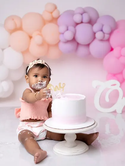 This one-year-old is enjoying her pastel-themed cake smash. The soft colors of the balloons and her outfit create a sweet and gentle look.