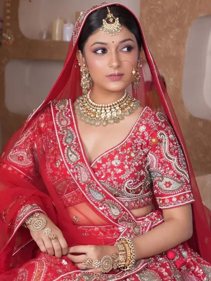 A classic red bridal look featuring a Kundan choker with light green bead drops, a matching maang tikka, and a traditional nath. This set is perfect for the quintessential Indian bride.