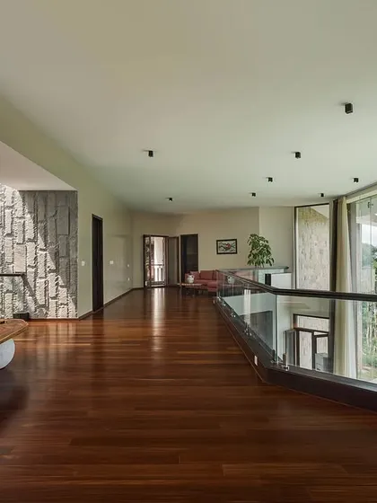 A wide corridor in the mountain home acts as a viewing gallery, with a glass railing ensuring uninterrupted views of the forest canopy. The wooden flooring and stone walls continue the theme of natural materials.