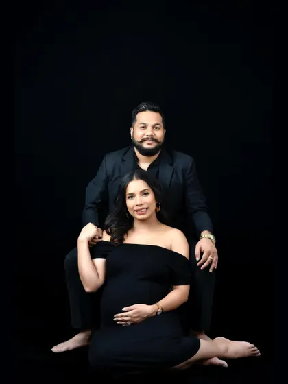 A classic black and white portrait of a couple against a solid black background. The simple, clean lighting creates a powerful and intimate image.