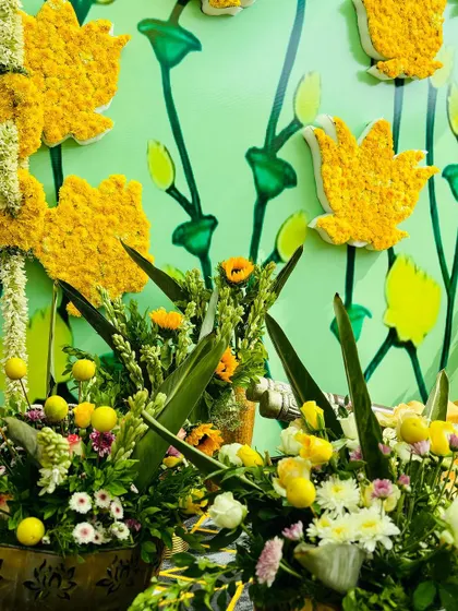 A detailed shot of the Haldi decor, featuring a custom floral wall with marigold lotuses and fresh green and yellow flower arrangements in brass pots.