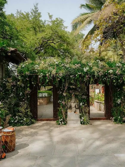The main gates are completely covered in lush greenery and white flowers, creating a magical, overgrown garden entrance for guests.