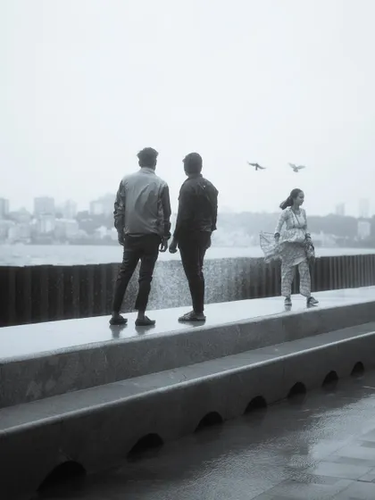 A black and white photo series capturing the spirit of Mumbai's monsoon at Marine Drive. People are seen enjoying the high tide, getting drenched by waves, and finding joy in the downpour.