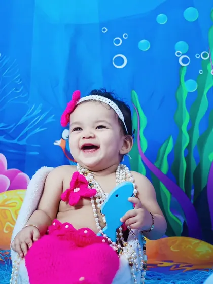 A joyful baby girl laughing during her pink mermaid-themed photoshoot.