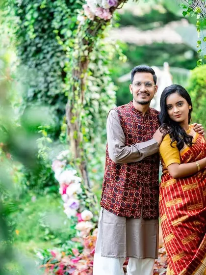 A classic portrait of a couple by a floral arch, with a soft, natural foreground.