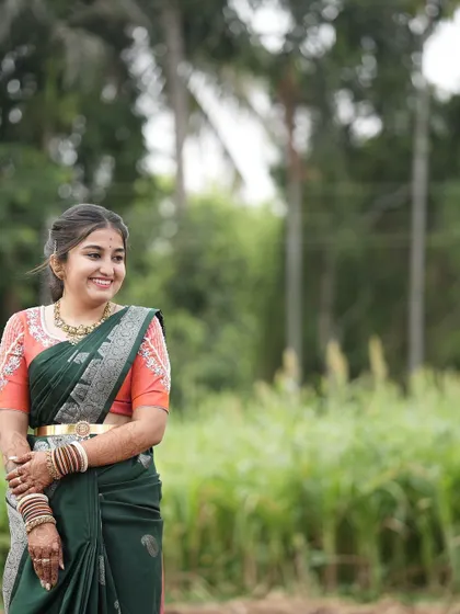 A beautiful bride in a dark green saree and a contrasting peach blouse with delicate pearl and thread work on the sleeves.