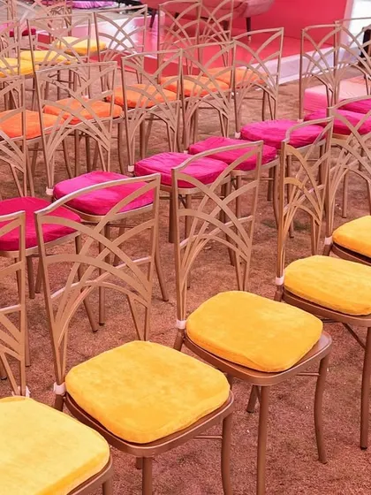 Rows of chairs with vibrant cushions in shades of pink, orange, and yellow, creating a beautiful gradient effect for guest seating.