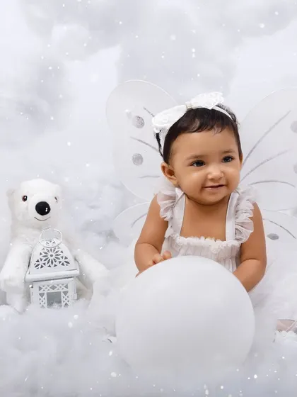 A sweet portrait of a baby girl dressed as an angel, sitting with a polar bear prop in a dreamy cloud setup.