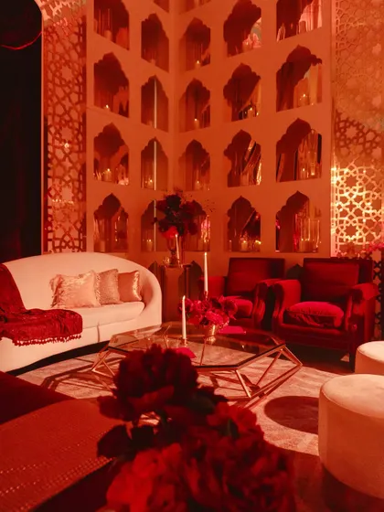 A cozy lounge area within the Sangeet venue, with red velvet armchairs and a wall of mirrored niches holding flickering candles.