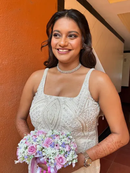 A beautiful portrait of the bride in her white wedding gown, holding a lovely bouquet. The makeup features cool purple tones for a soft, romantic glam.