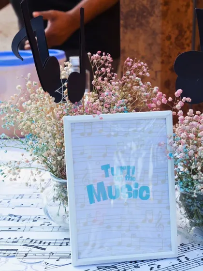 A "Turn Up the Music" sign sits on a table covered with a musical note runner, surrounded by delicate baby's breath. It's these small, thematic details that create a cohesive atmosphere.