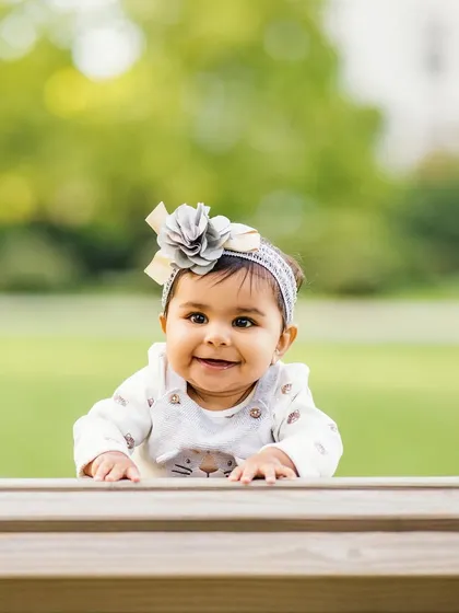 Peek-a-boo. A playful shot of a curious and happy baby peeking over a wooden bench outdoors. Her bright smile can light up any day.