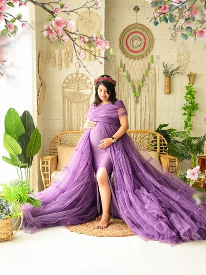 A serene solo portrait of the mom-to-be in a flowing purple gown. This shot highlights our boho set, complete with a rattan bench, floral accents, and macrame wall decor.