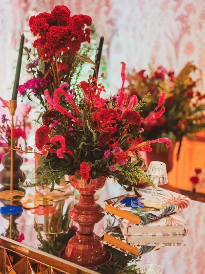 A close-up of the sangeet bar decor, with rich red floral arrangements, vintage books, and a miniature lamp adding layers of detail and sophistication.