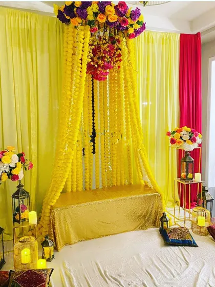 An intimate indoor Haldi or Mehendi seating area. The canopy of marigolds and the surrounding lanterns create a cozy and warm atmosphere.