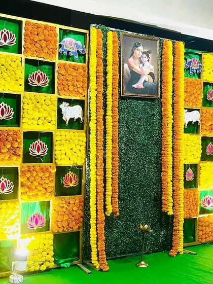 A closer view of a traditional Seemantham backdrop. The design incorporates marigolds, lotus motifs, and auspicious symbols like cows and elephants, all framing a central portrait of mother and child.