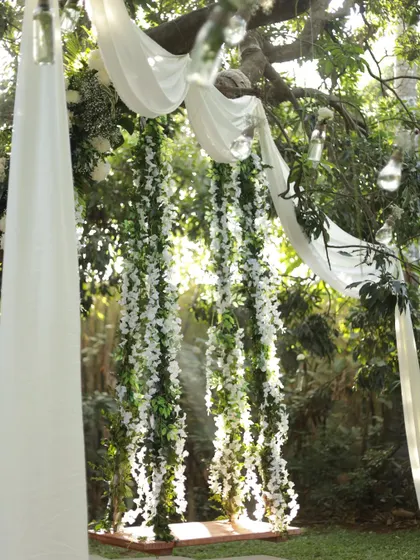 A romantic floral swing draped in white fabric and adorned with hanging white orchids, perfect for dreamy photos.