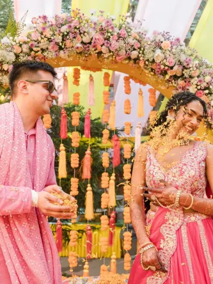 The groom showers his bride with a handful of marigold petals, and her laughing reaction is priceless. This is a perfect candid moment of love and playfulness.