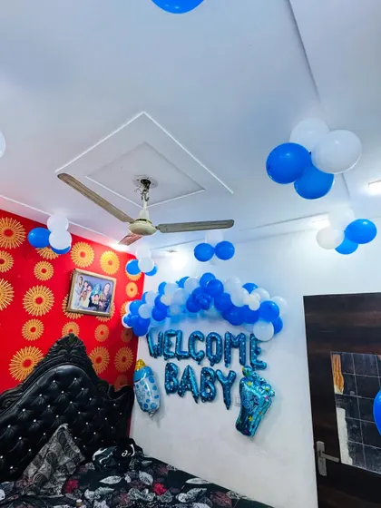 A wider view of the room decorated to welcome a baby boy, with balloons on the ceiling and a main backdrop on the wall.