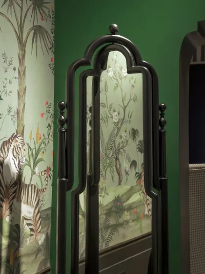 A custom-designed mirror with a traditional, ornate black frame, reflecting a vibrant, tropical-themed wallpaper. Our pieces are designed to complement and enhance their surroundings.