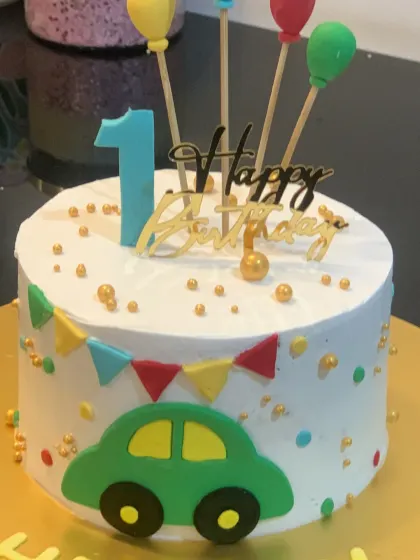 A sweet and simple car cake for a first birthday. The white cake is decorated with a colorful bunting, sprinkles, and a cute green car.